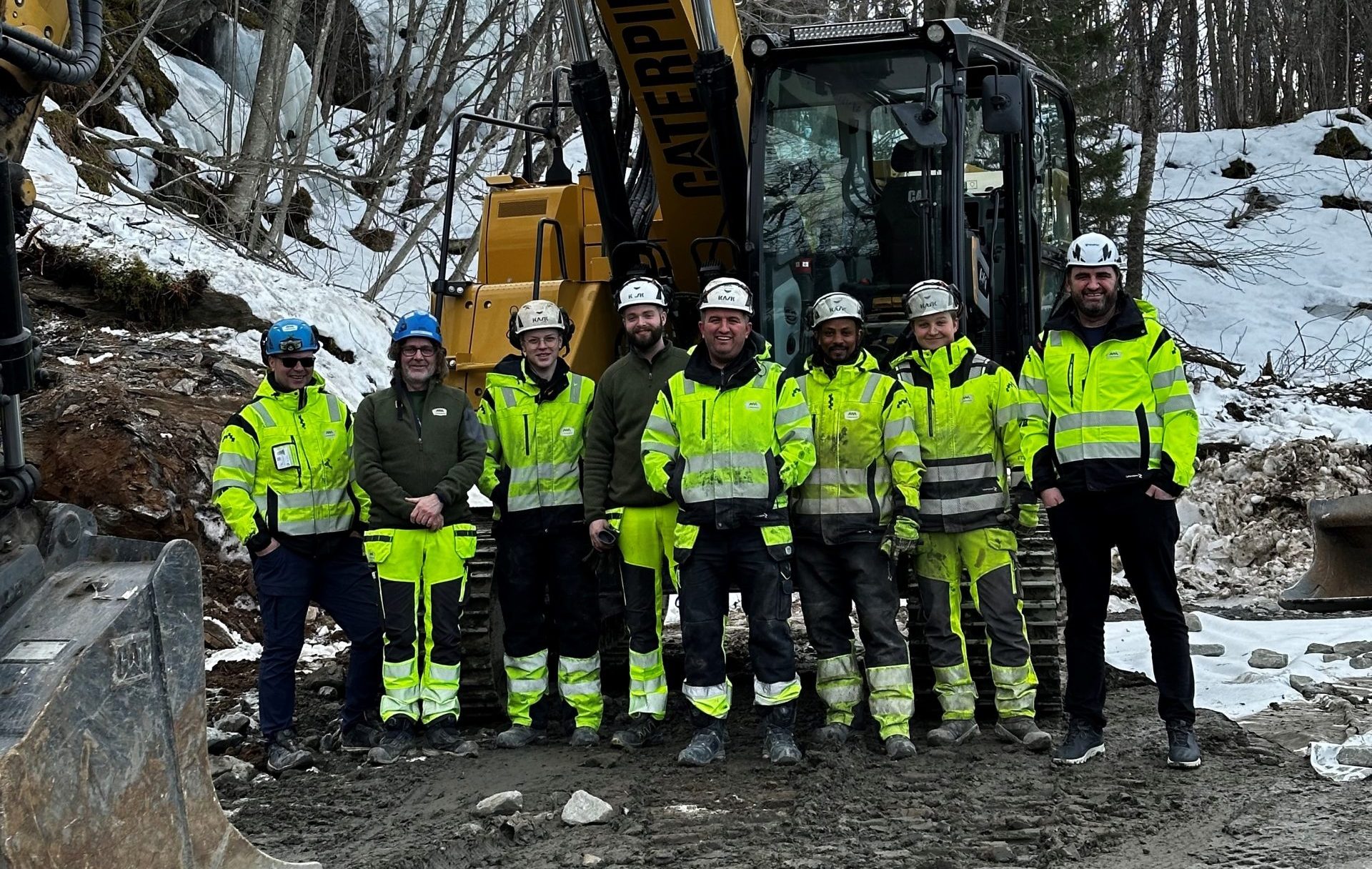 a group of men in safety jackets and helmets standing in front of a construction vehicle